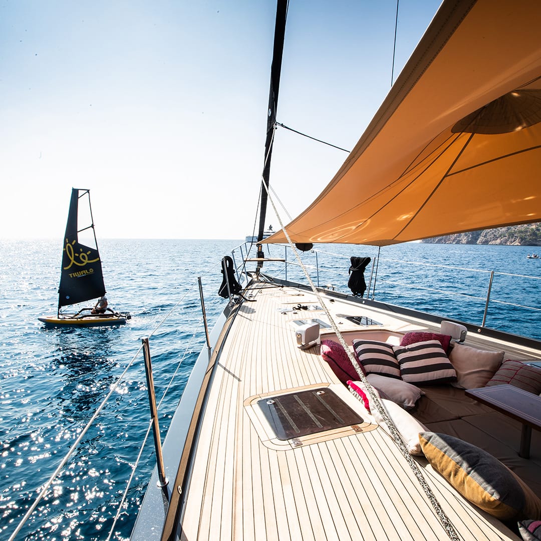 Tiwal small sailing dinghy cruising upfront an Oyster yacht